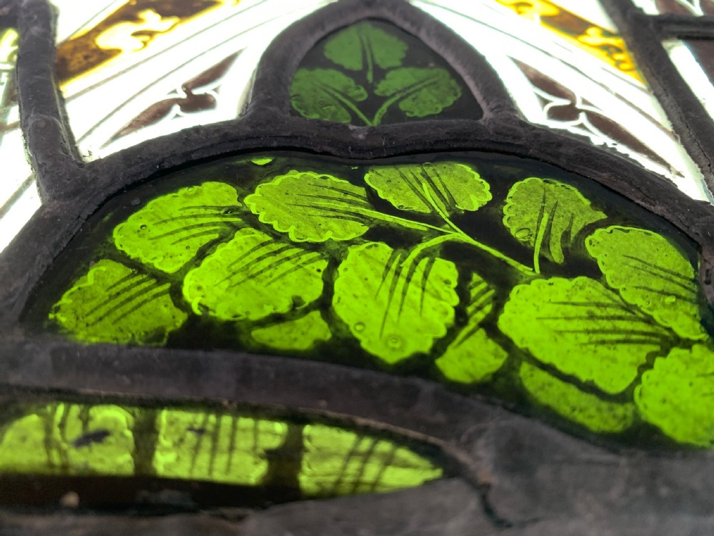 An arched Gothic Revival stained glass panel featuring painted architectural spires, foliate patterns, and lead cames in red, green, yellow, and clear glass. View IX