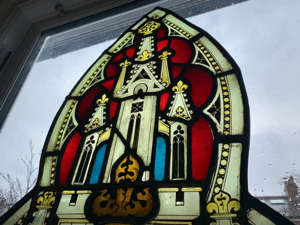An arched Gothic Revival stained glass panel featuring painted architectural spires, foliate patterns, and lead cames in red, green, yellow, and clear glass. View X