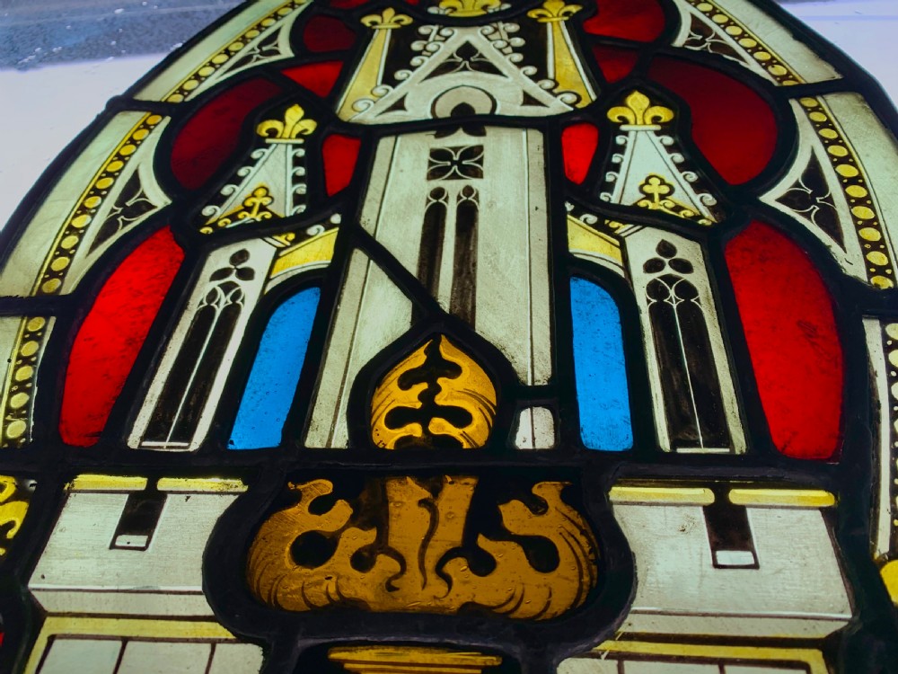 An arched Gothic Revival stained glass panel featuring painted architectural spires, foliate patterns, and lead cames in red, green, yellow, and clear glass. View XI