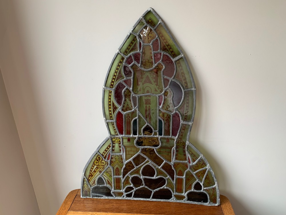 An arched Gothic Revival stained glass panel featuring painted architectural spires, foliate patterns, and lead cames in red, green, yellow, and clear glass. View XII
