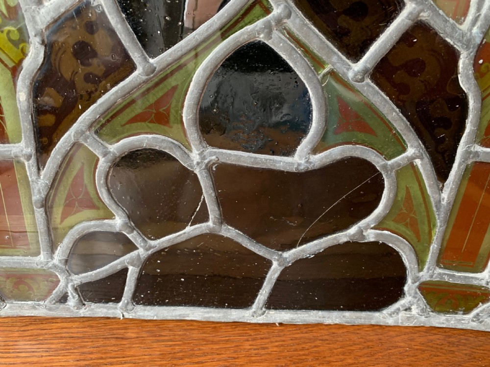 An arched Gothic Revival stained glass panel featuring painted architectural spires, foliate patterns, and lead cames in red, green, yellow, and clear glass. View XIII