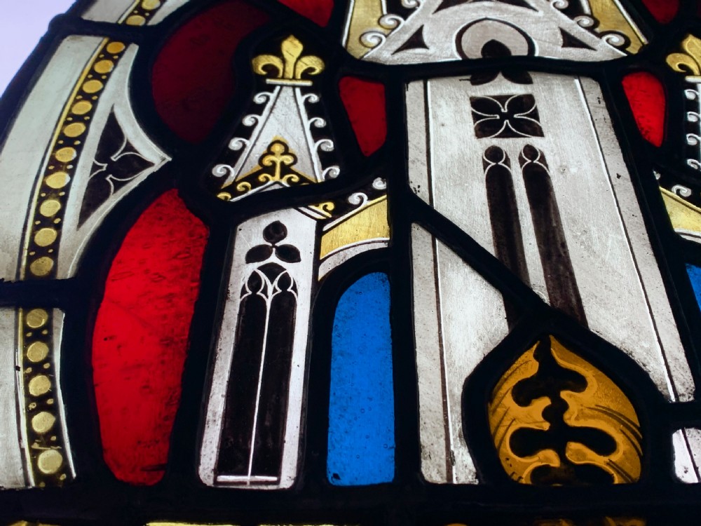 An arched Gothic Revival stained glass panel featuring painted architectural spires, foliate patterns, and lead cames in red, green, yellow, and clear glass. View XV