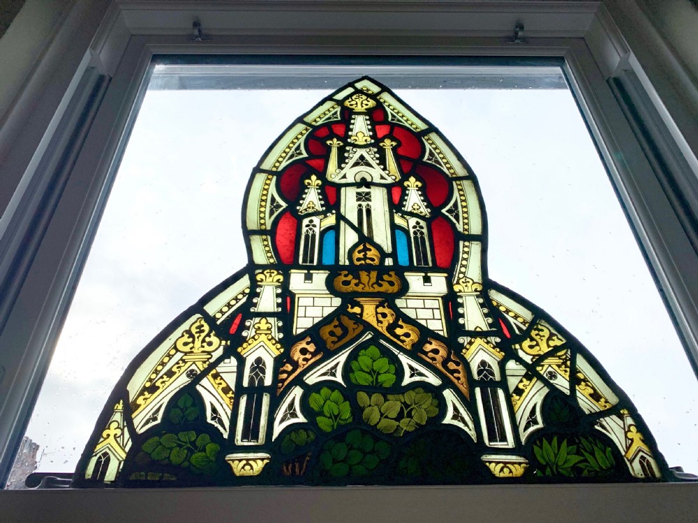 An arched Gothic Revival stained glass panel featuring painted architectural spires, foliate patterns, and lead cames in red, green, yellow, and clear glass. View XVI