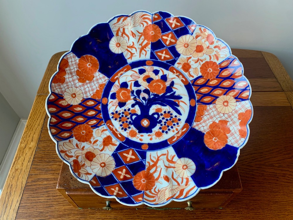 A nineteenth-century Japanese Imari porcelain charger featuring a scalloped rim, hand-painted in cobalt blue and iron-red floral and geometric brocade panels.