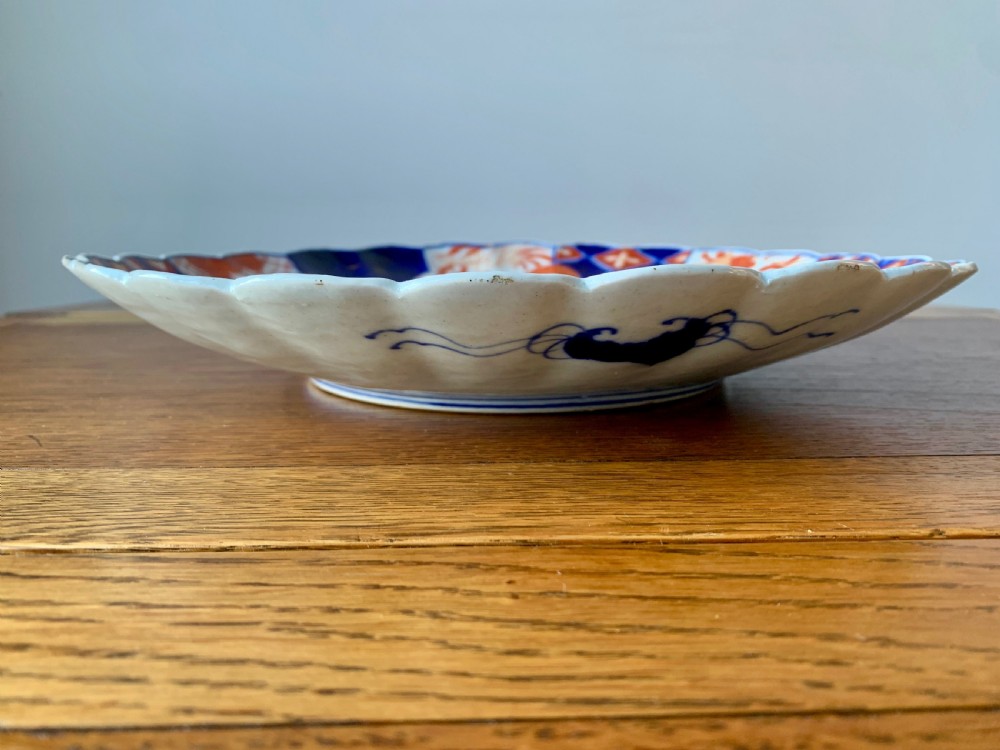 A nineteenth-century Japanese Imari porcelain charger featuring a scalloped rim, hand-painted in cobalt blue and iron-red floral and geometric brocade panels. View IX