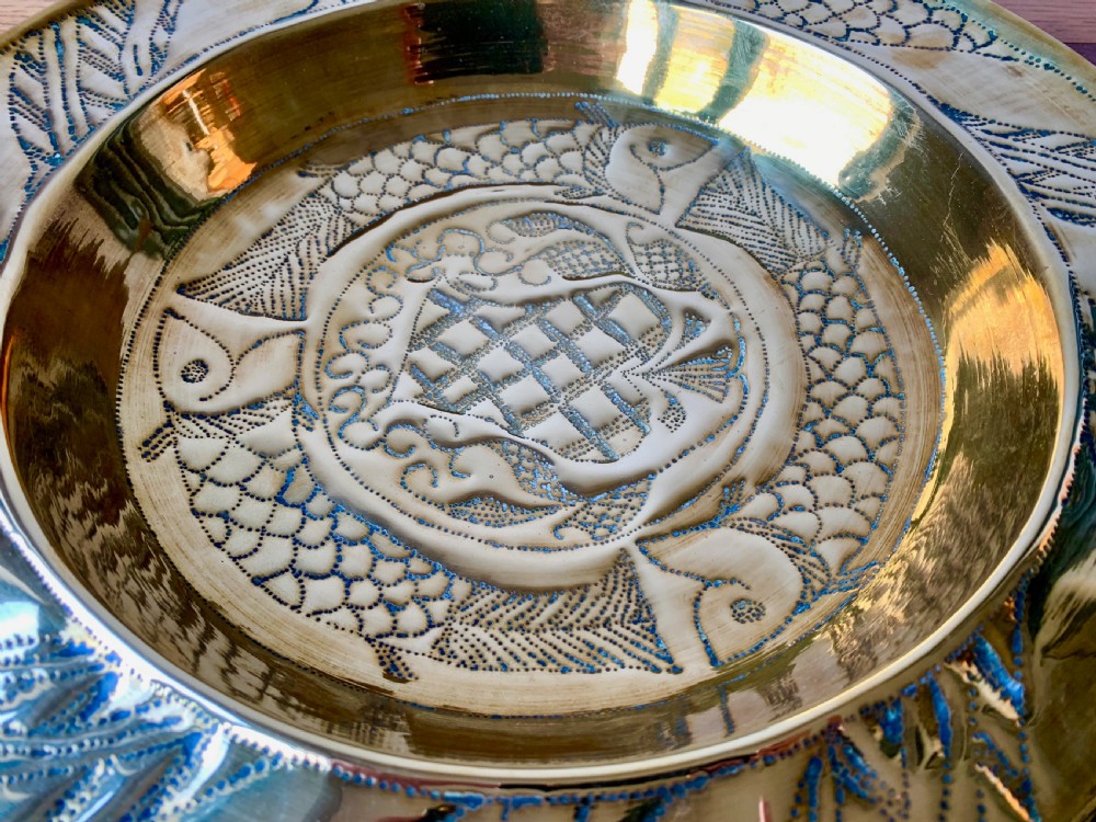 A circular Arts and Crafts hand-hammered brass charger featuring repousse decoration of three fish surrounding a central fountain design. View III