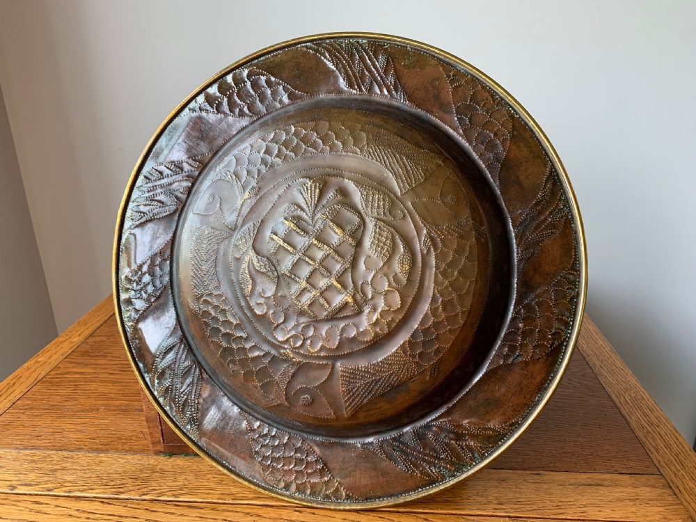 A circular Arts and Crafts hand-hammered brass charger featuring repousse decoration of three fish surrounding a central fountain design. View V