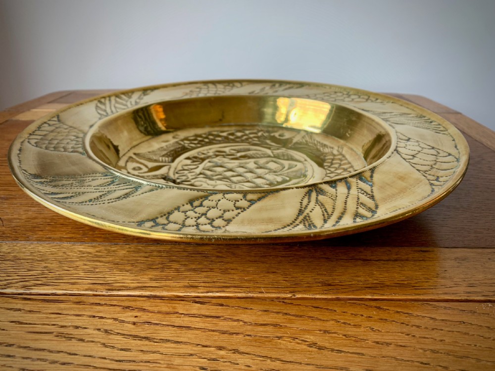 A circular Arts and Crafts hand-hammered brass charger featuring repousse decoration of three fish surrounding a central fountain design. View VI
