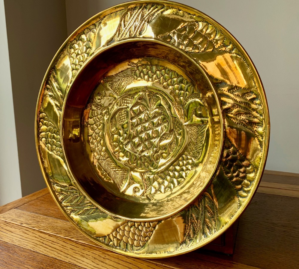 A circular Arts and Crafts hand-hammered brass charger featuring repousse decoration of three fish surrounding a central fountain design. View VII