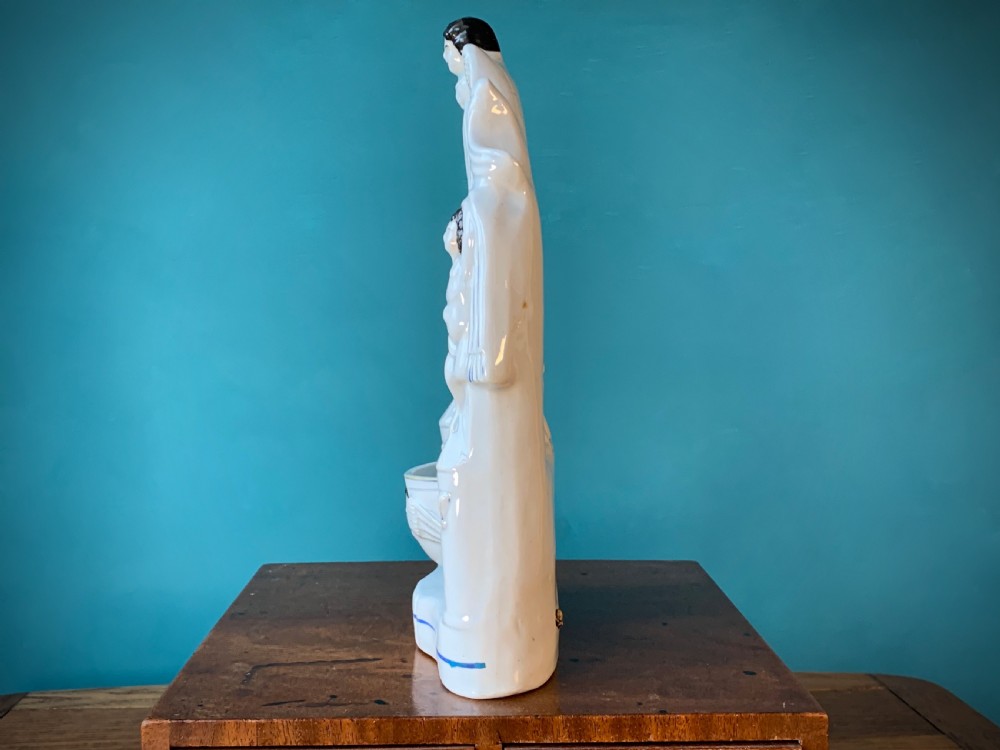 An antique Staffordshire earthenware holy water stoup with figures of the Madonna and Child under an arch flanked by angels in cream glaze with blue and brown painted details. View IV