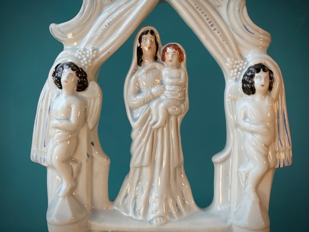 An antique Staffordshire earthenware holy water stoup with figures of the Madonna and Child under an arch flanked by angels in cream glaze with blue and brown painted details. View V