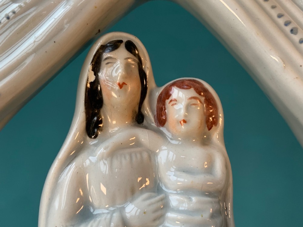 An antique Staffordshire earthenware holy water stoup with figures of the Madonna and Child under an arch flanked by angels in cream glaze with blue and brown painted details. View VII
