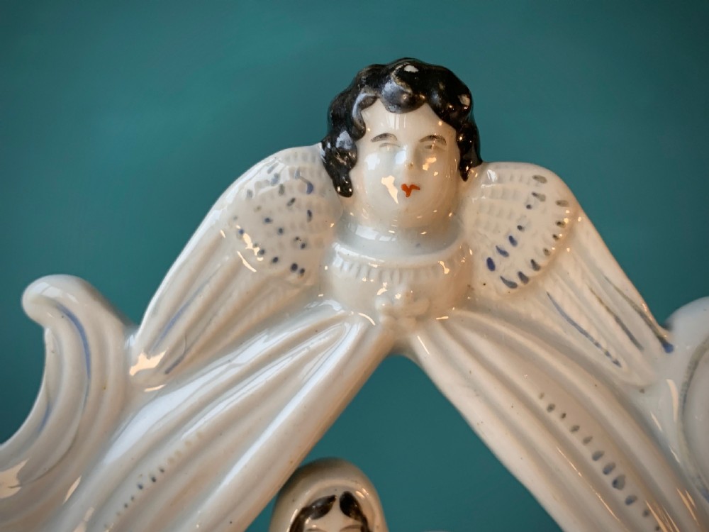An antique Staffordshire earthenware holy water stoup with figures of the Madonna and Child under an arch flanked by angels in cream glaze with blue and brown painted details. View VIII