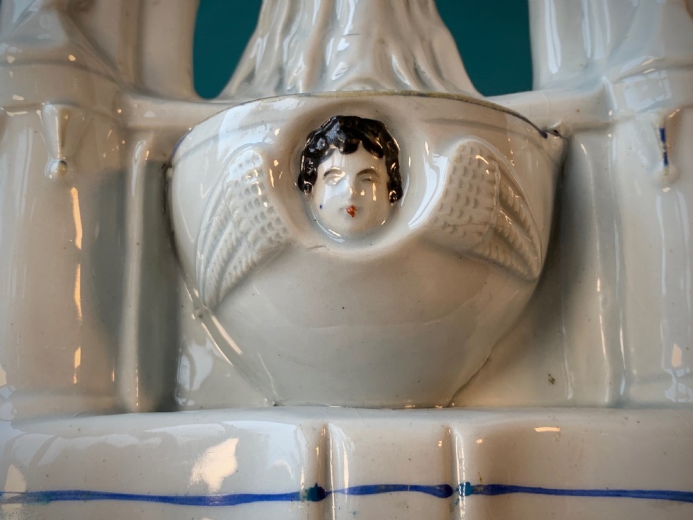 An antique Staffordshire earthenware holy water stoup with figures of the Madonna and Child under an arch flanked by angels in cream glaze with blue and brown painted details. View IX