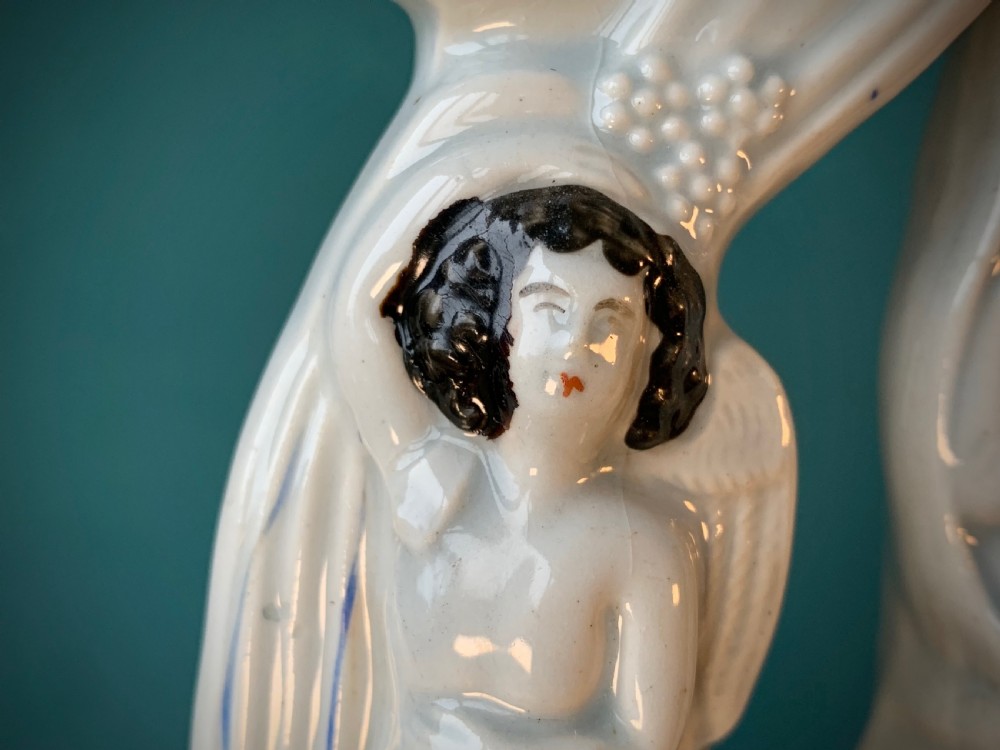 An antique Staffordshire earthenware holy water stoup with figures of the Madonna and Child under an arch flanked by angels in cream glaze with blue and brown painted details. View X