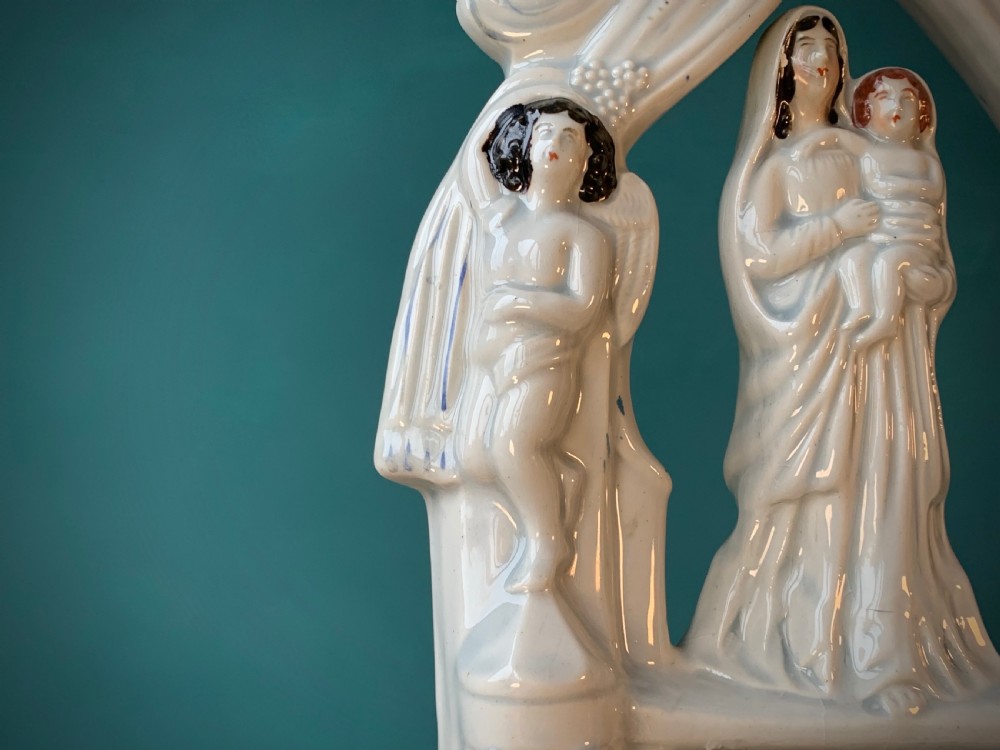 An antique Staffordshire earthenware holy water stoup with figures of the Madonna and Child under an arch flanked by angels in cream glaze with blue and brown painted details. View XII