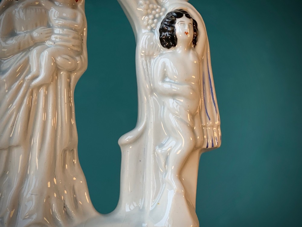 An antique Staffordshire earthenware holy water stoup with figures of the Madonna and Child under an arch flanked by angels in cream glaze with blue and brown painted details. View XIII