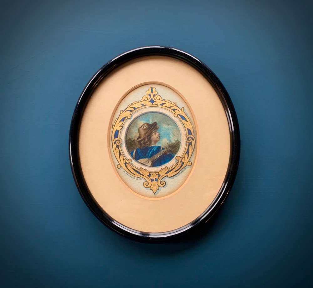 An oval framed miniature watercolour painting depicting a travelling musician wearing a blue tunic and feathered hat, surrounded by an ornate gilded and blue cartouche border.