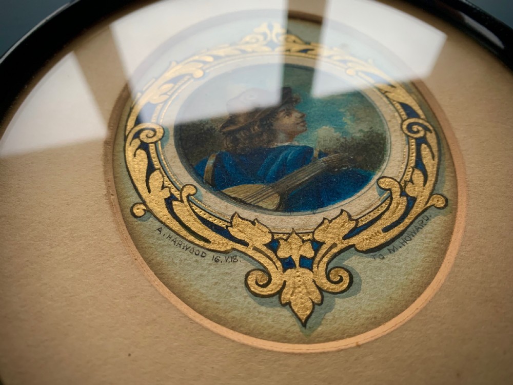 An oval framed miniature watercolour painting depicting a travelling musician wearing a blue tunic and feathered hat, surrounded by an ornate gilded and blue cartouche border. View III