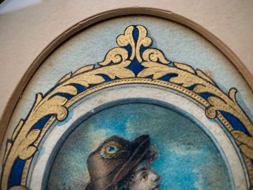 An oval framed miniature watercolour painting depicting a travelling musician wearing a blue tunic and feathered hat, surrounded by an ornate gilded and blue cartouche border. View VI