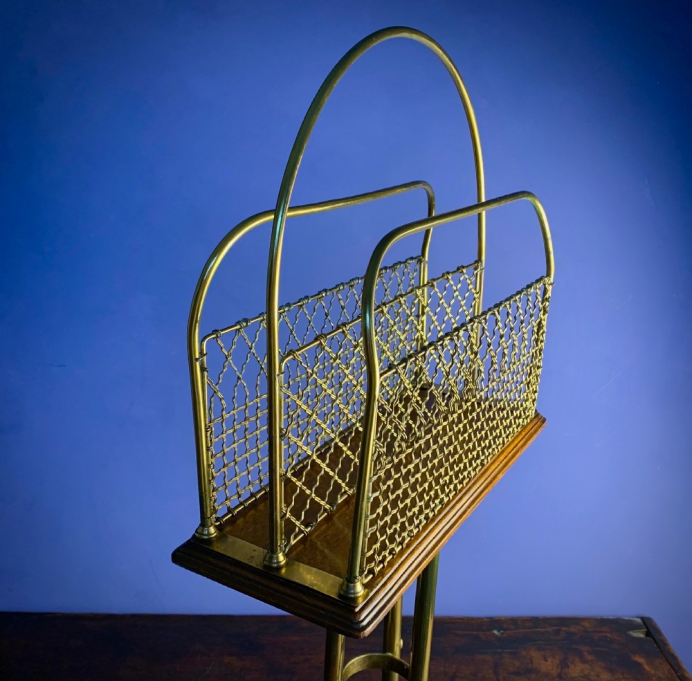 A Victorian tubular brass magazine stand featuring mesh wire compartments, a central carrying handle, and a mahogany base supported by splayed legs. View III