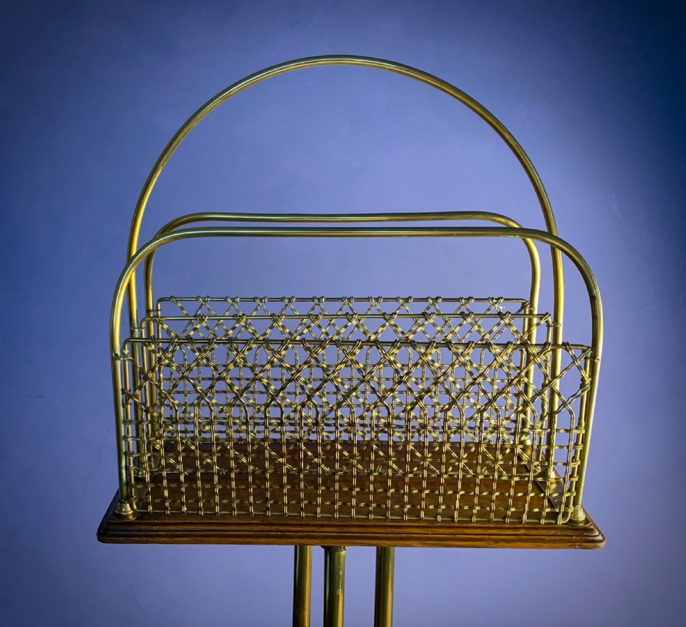 A Victorian tubular brass magazine stand featuring mesh wire compartments, a central carrying handle, and a mahogany base supported by splayed legs. View VII