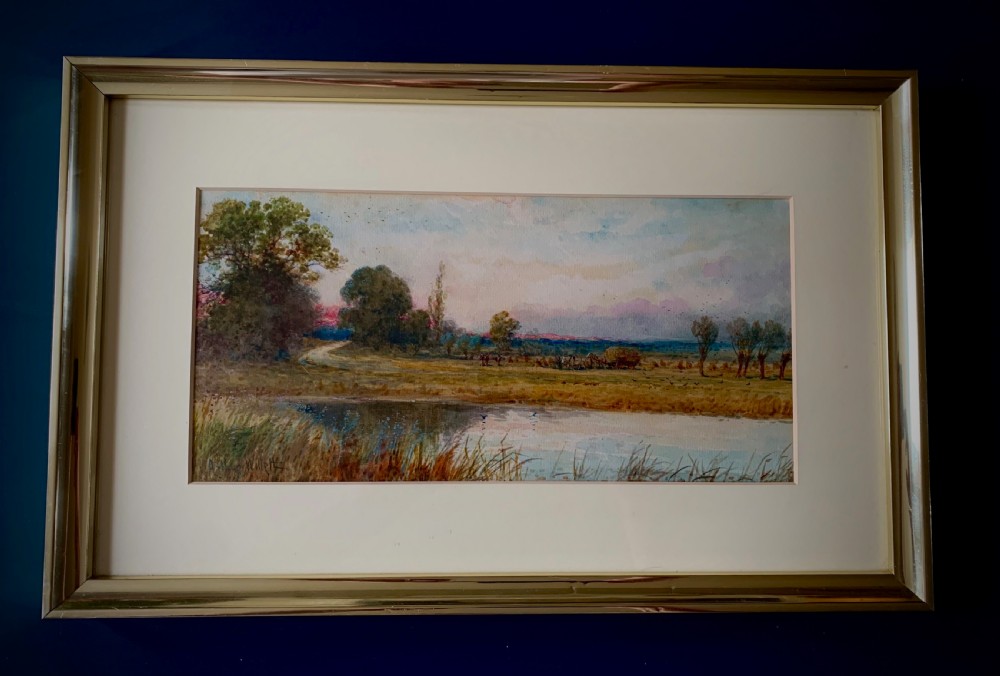 A framed 19th-century watercolour painting depicting a serene rural sunset landscape with a calm river, trees, and fields.