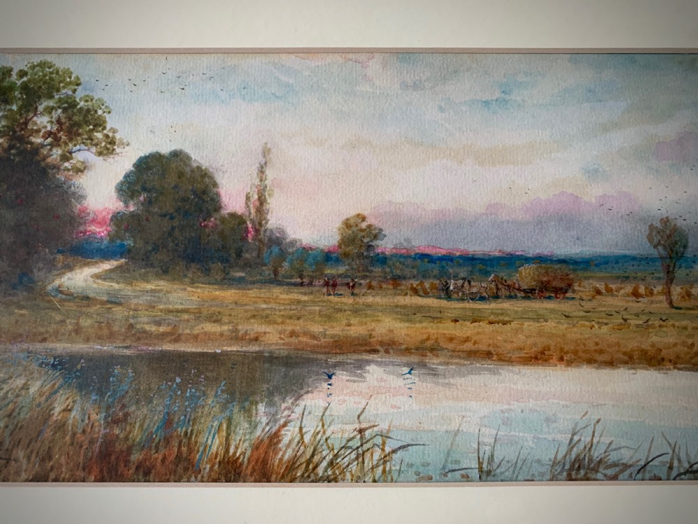 A framed 19th-century watercolour painting depicting a serene rural sunset landscape with a calm river, trees, and fields. View II