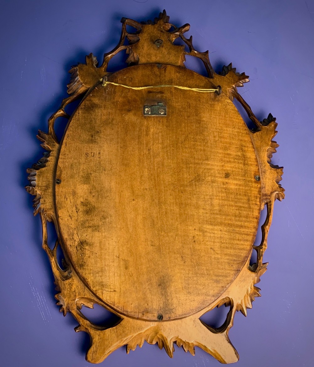 An early 20th-century oval wall mirror featuring a carved wooden frame decorated with grapevines, leaves, and branch motifs around a bevelled glass mirror plate. View VI