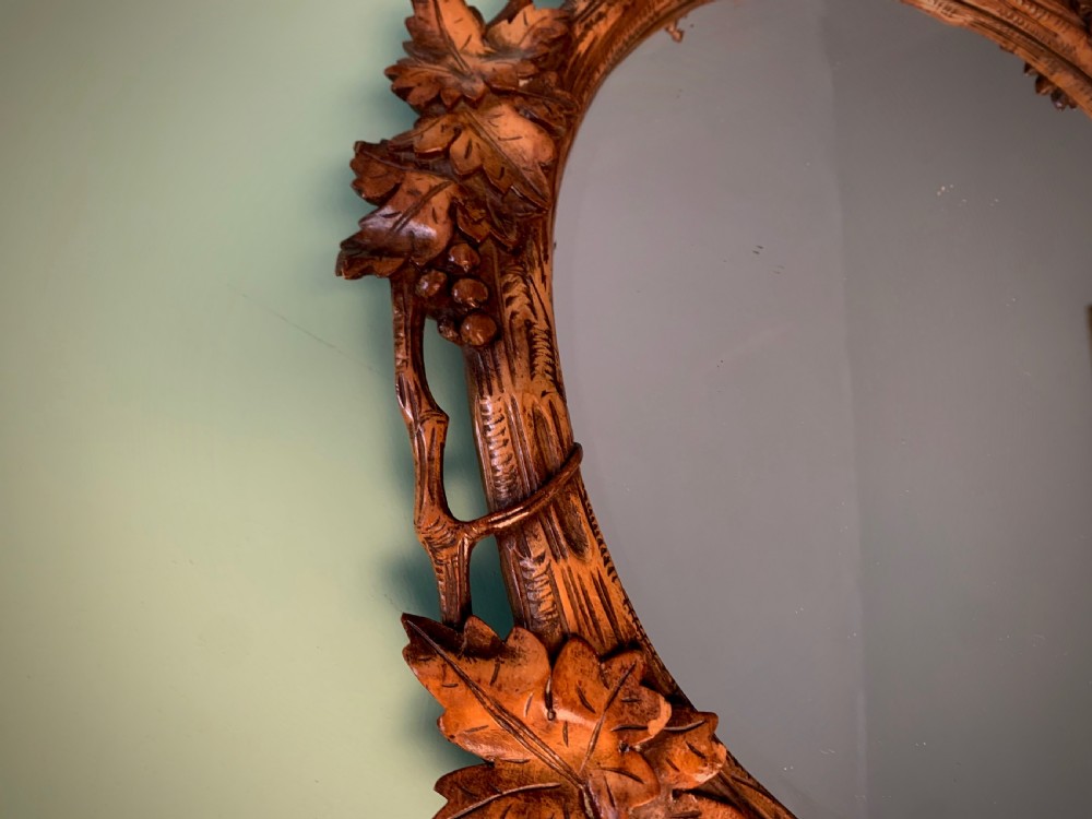 An early 20th-century oval wall mirror featuring a carved wooden frame decorated with grapevines, leaves, and branch motifs around a bevelled glass mirror plate. View VIII