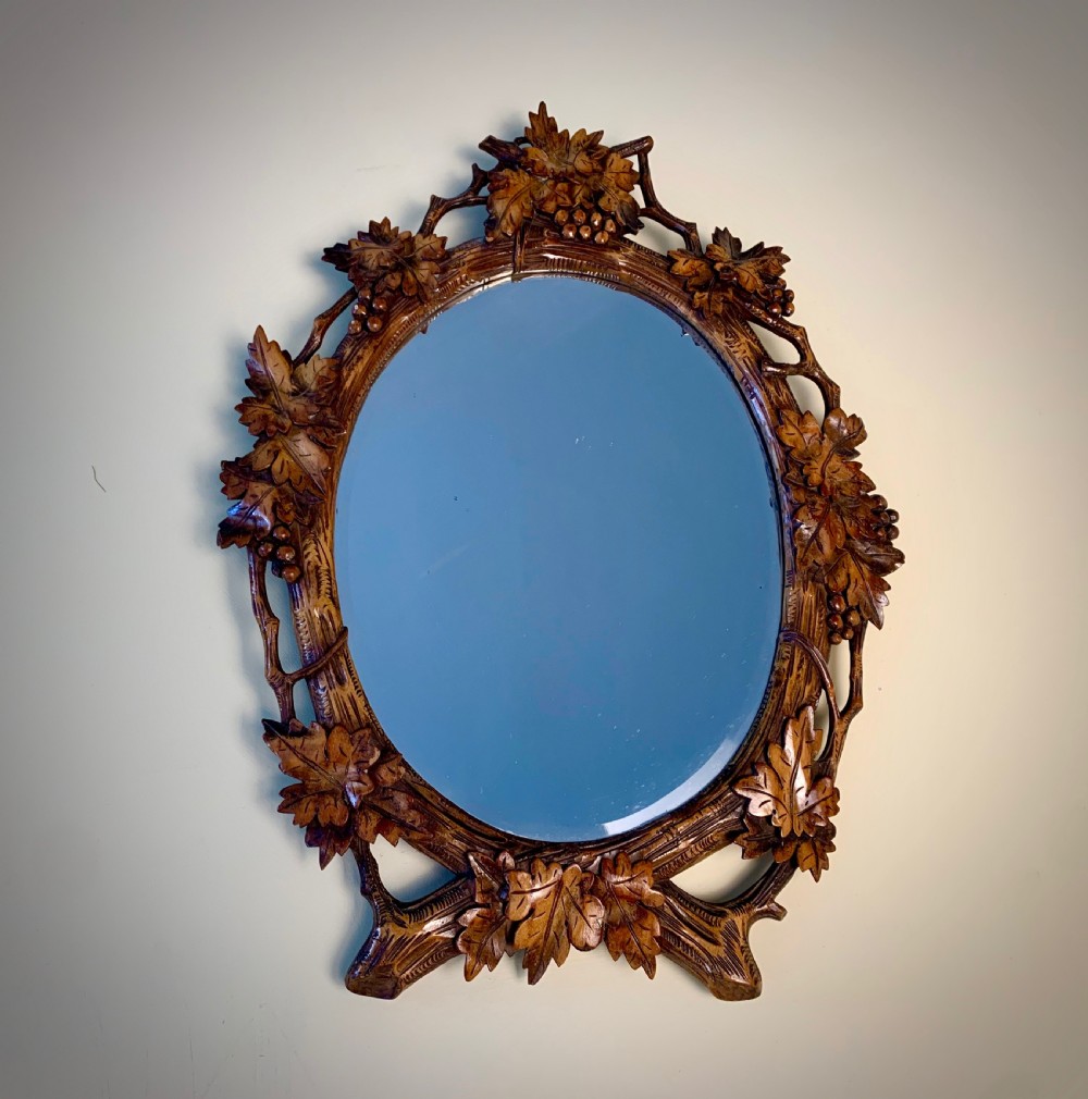 An early 20th-century oval wall mirror featuring a carved wooden frame decorated with grapevines, leaves, and branch motifs around a bevelled glass mirror plate. View IX