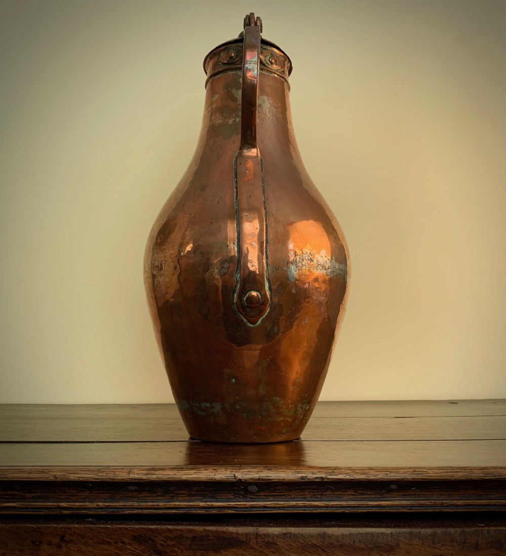 A large hand-hammered copper pitcher featuring a tapered neck, rounded body, strap handle, and a hinged lid. View IV