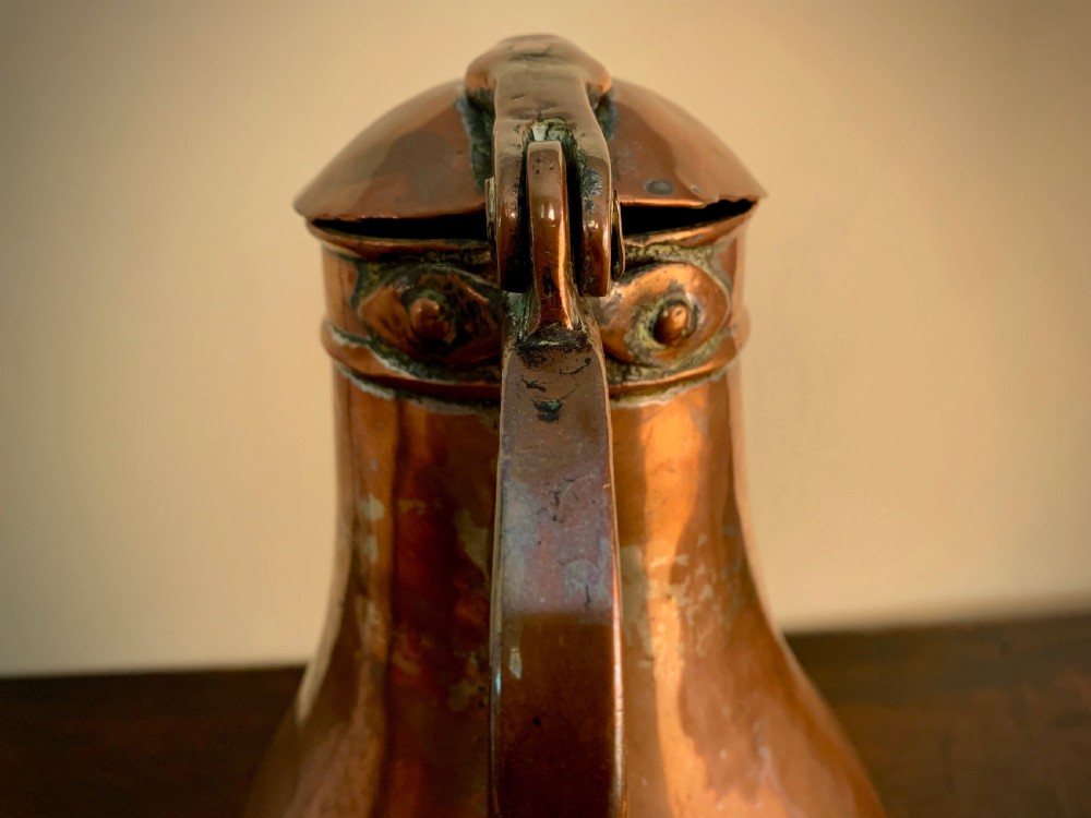 A large hand-hammered copper pitcher featuring a tapered neck, rounded body, strap handle, and a hinged lid. View IX