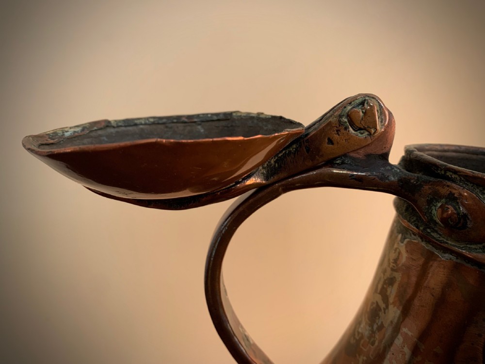 A large hand-hammered copper pitcher featuring a tapered neck, rounded body, strap handle, and a hinged lid. View XI