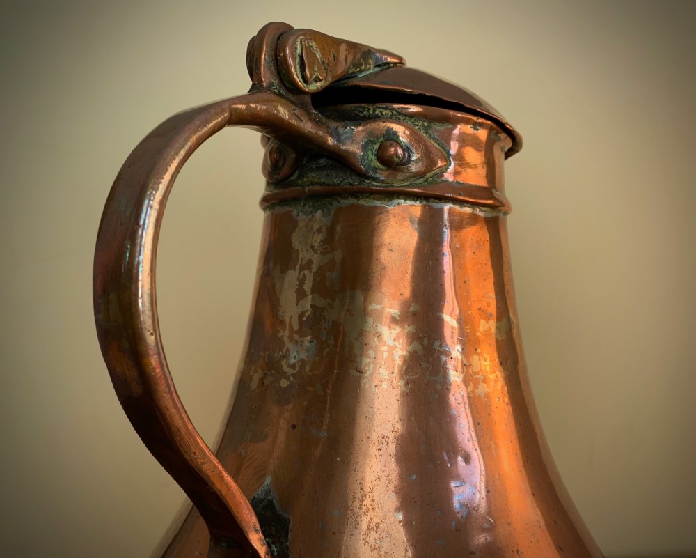 A large hand-hammered copper pitcher featuring a tapered neck, rounded body, strap handle, and a hinged lid. View XIV