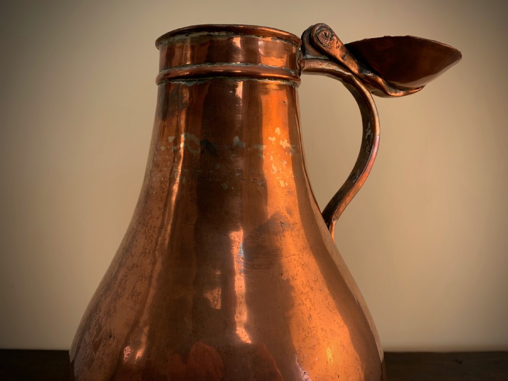 A large hand-hammered copper pitcher featuring a tapered neck, rounded body, strap handle, and a hinged lid. View XVI