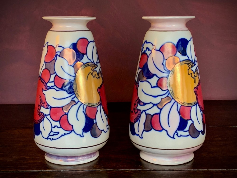 A pair of Art Deco earthenware vases featuring tubelined fruit motifs with iridescent lustre glazing on a cream background.