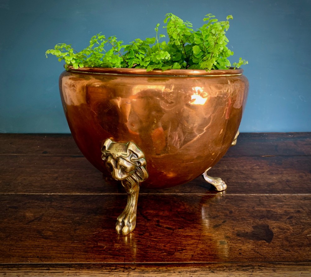 A rounded nineteenth-century copper jardiniere bowl supported on three cast brass lion mask paw feet.