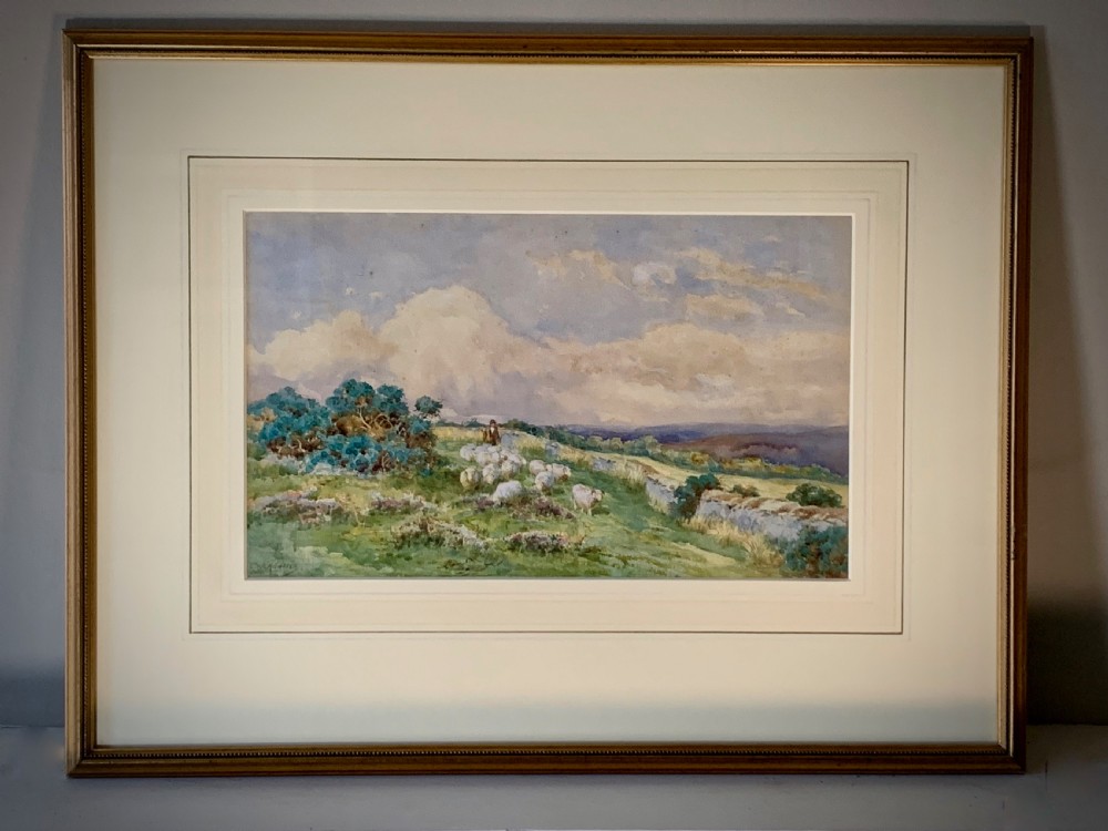 An antique framed watercolour painting depicting a shepherd driving sheep across a green moorland beneath a cloudy sky, set within a cream mount and gold frame.