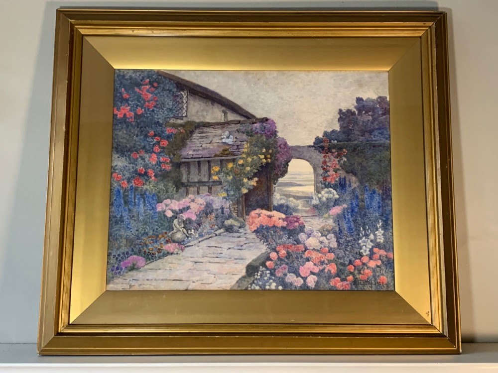 A framed 1928 watercolour painting depicting a stone path leading through a lush cottage garden towards a stone archway, presented in a wide gold frame.