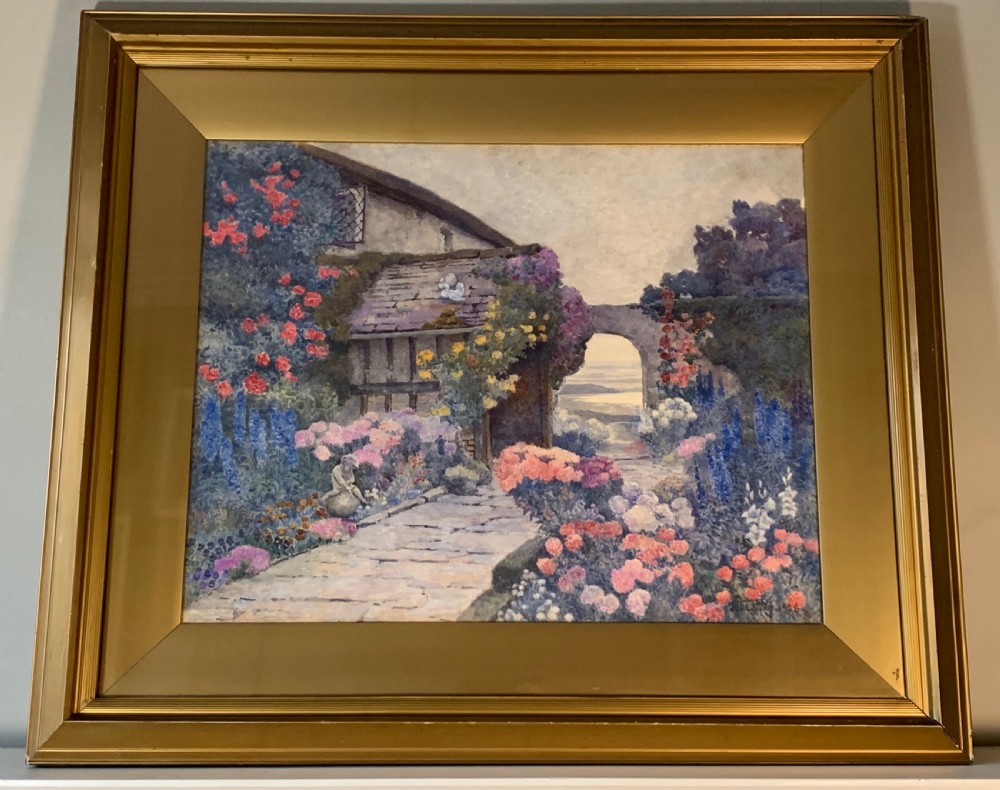 A framed 1928 watercolour painting depicting a stone path leading through a lush cottage garden towards a stone archway, presented in a wide gold frame. View VII
