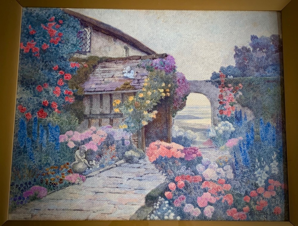 A framed 1928 watercolour painting depicting a stone path leading through a lush cottage garden towards a stone archway, presented in a wide gold frame. View X
