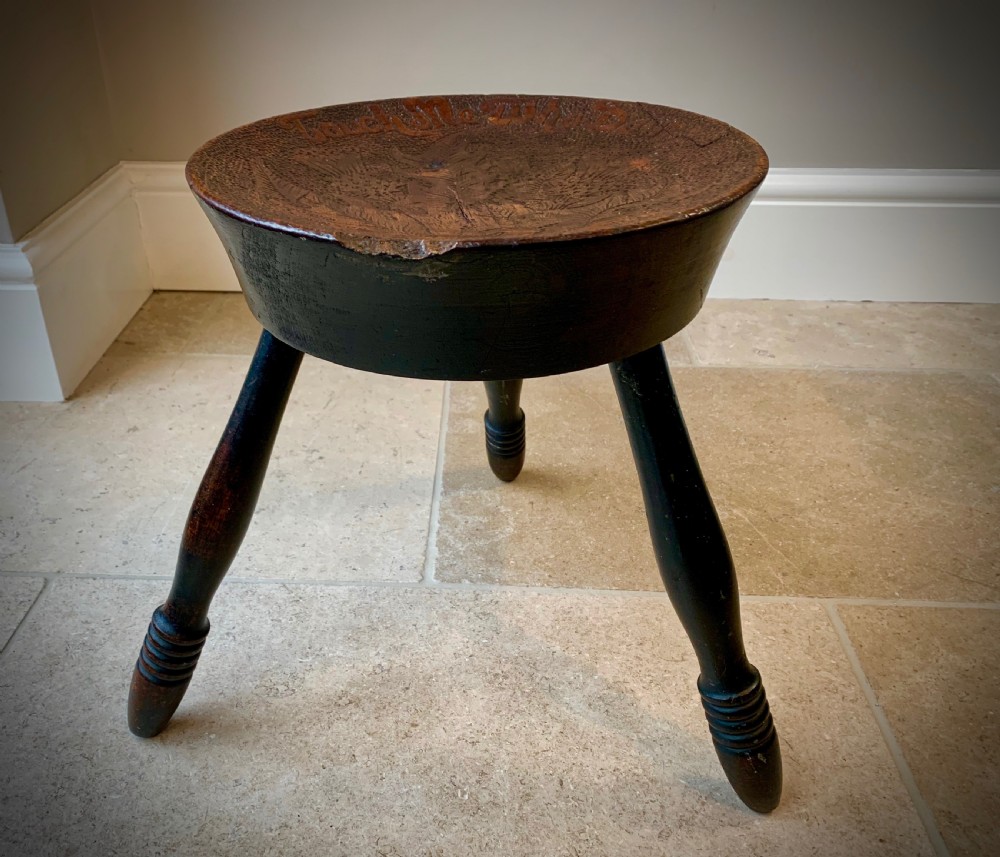A 19th-century Scottish tripod stool crafted from dark brown wood with a circular seat featuring burnt pokerwork text and a Scottish thistle motif.