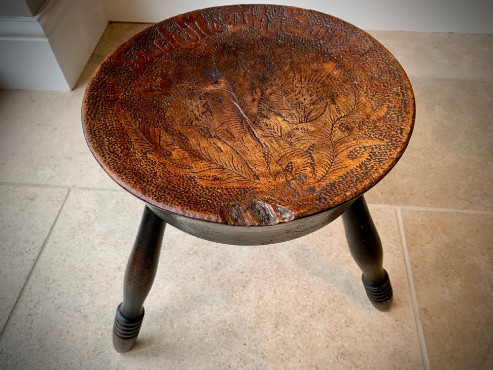 A 19th-century Scottish tripod stool crafted from dark brown wood with a circular seat featuring burnt pokerwork text and a Scottish thistle motif. View III
