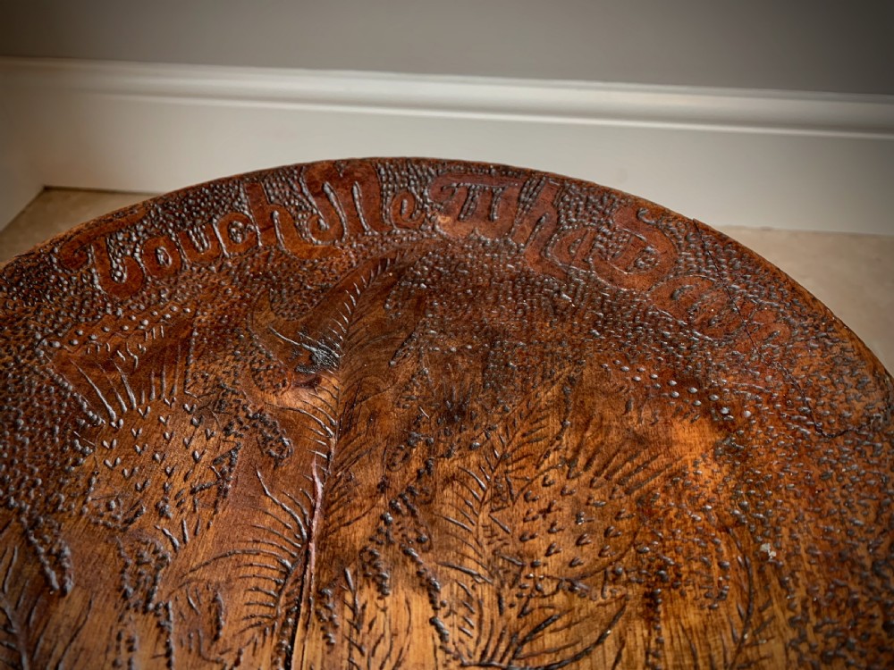 A 19th-century Scottish tripod stool crafted from dark brown wood with a circular seat featuring burnt pokerwork text and a Scottish thistle motif. View VIII
