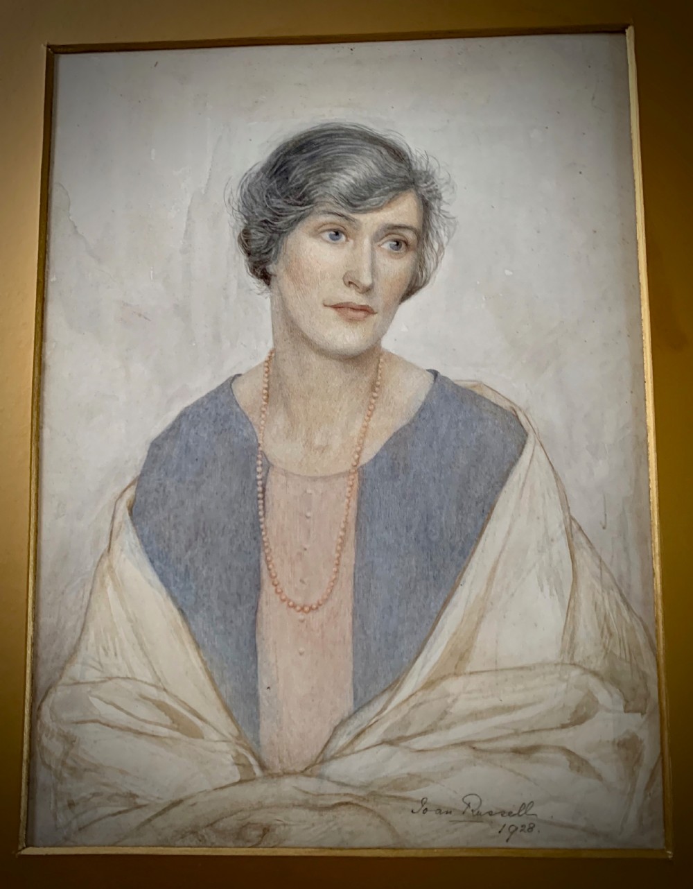 A framed 1928 watercolour painting of a young woman with short dark hair, wearing a blue jacket and shawl, set within a wide gold mount and ornate gilded frame. View II