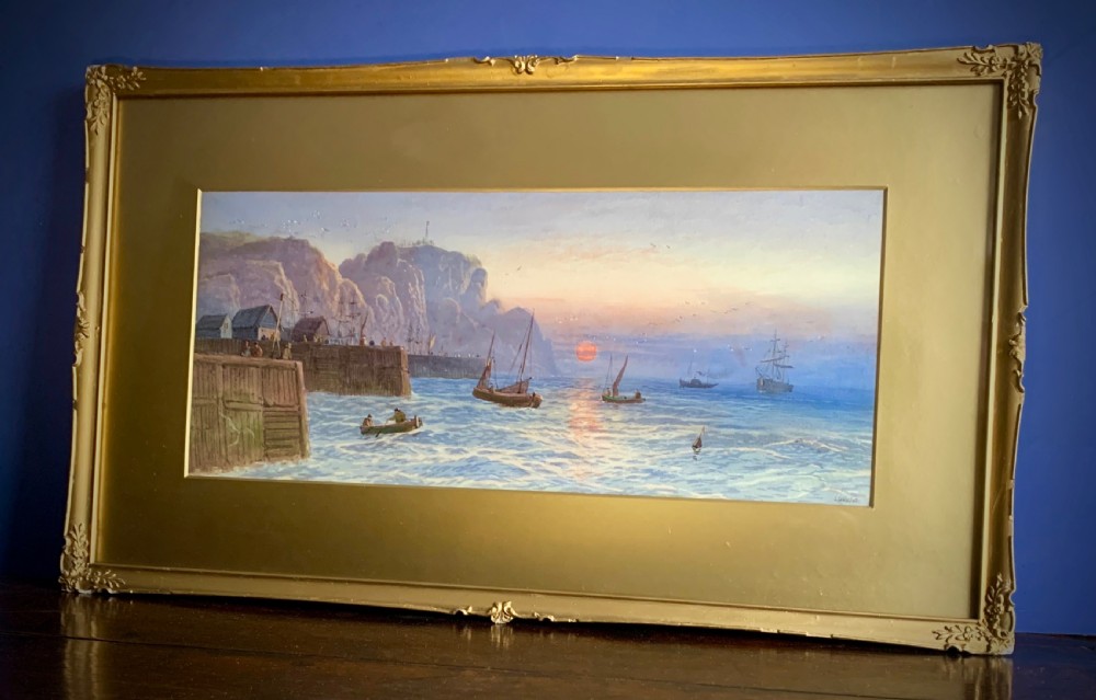 A horizontal Victorian watercolour painting depicting sailing boats in a coastal harbour at sunset, set within a wide gilded frame.