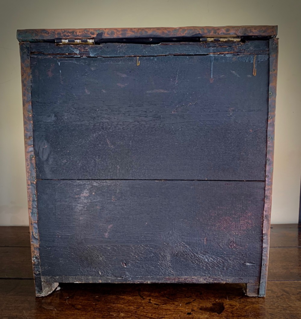 A hand-hammered copper log box featuring an embossed stylised floral motif on the sloping lid and front panel, secured with riveted corner straps. View VII