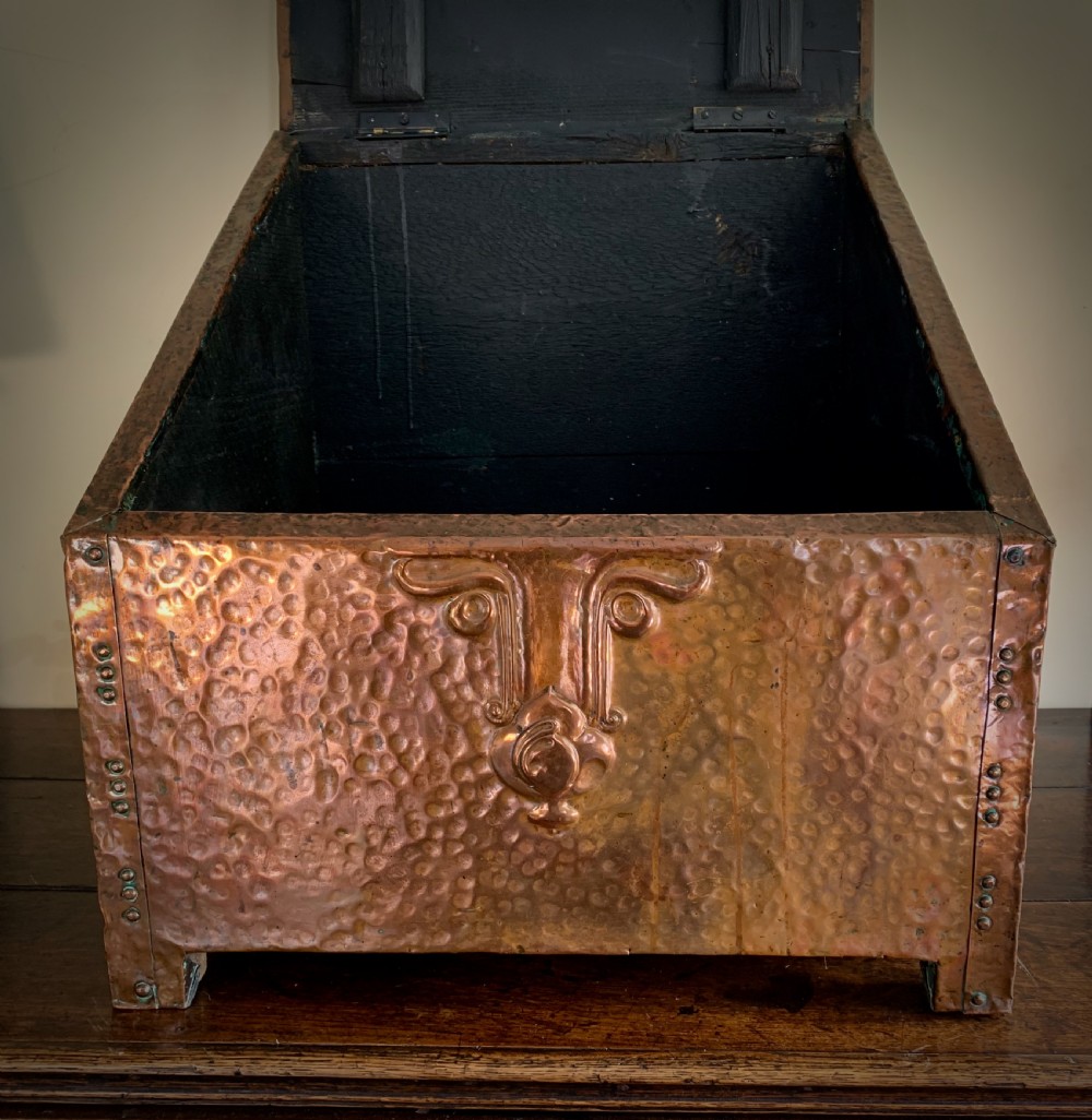 A hand-hammered copper log box featuring an embossed stylised floral motif on the sloping lid and front panel, secured with riveted corner straps. View VIII