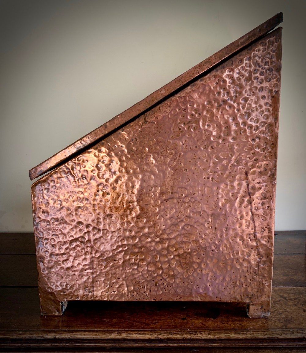 A hand-hammered copper log box featuring an embossed stylised floral motif on the sloping lid and front panel, secured with riveted corner straps. View XII